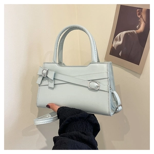 Detailed view of mint blue handbag featuring a bow metal buckle and cross straps