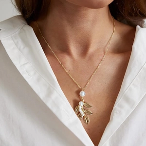 Gros plan détaillé d'un pendentif feuille dorée avec cinq perles sur un collier mariée