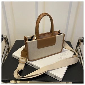 Detail of canvas and brown leather crossbody bag featuring wide webbing strap and gold hardware