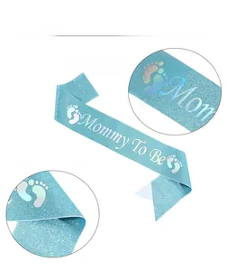 Close-up of blue glitter Mommy To Be sash with colorful laser lettering and footprints