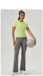 Femme en t-shirt de yoga vert néon et legging évasé gris posant avec un ballon de fitness