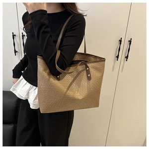 Detailed shot of large khaki woven tote bag with leather straps on model's shoulder