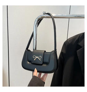 Detail of elegant black leather handbag featuring a golden bow-knot buckle on silver rack