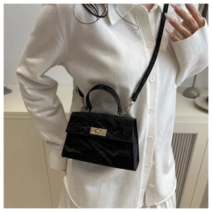 Detail of a vintage black wrinkled square bag with golden lock on a white shirt