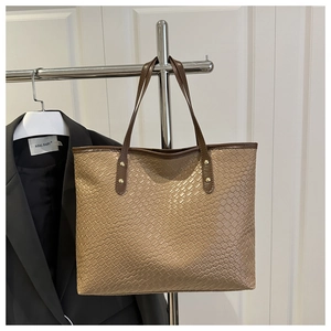 Detail of woven leather texture and sturdy rivet handles on large khaki tote bag