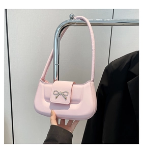 Detail of pink faux leather shoulder bag with golden bow clasp and slender strap