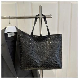 Close-up of black woven leather tote bag with metallic rivet details on handle straps