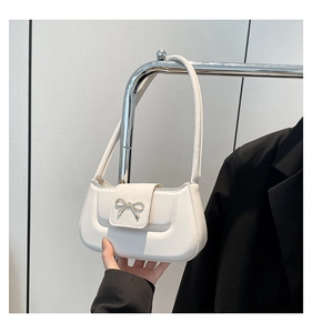 Close-up of a white faux leather underarm bag featuring a gold metal bow on the front
