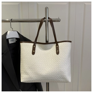 Close-up of white woven tote bag featuring brown straps and metallic gold rivet details