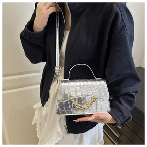 Détails de texture crocodile et chaîne dorée sur sac argenté porté en bandoulière