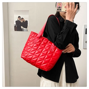 Detail view of red quilted stitching on a high-gloss nylon tote bag with webbing handles