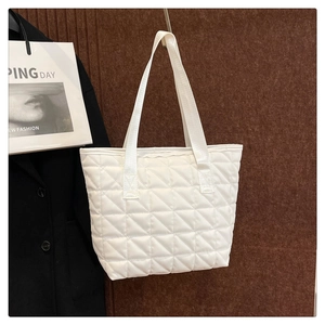 Detail of white quilted tote bag featuring classic diamond stitching and flat handles