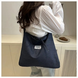 Deep blue denim tote bag with FASHION label shown on model's shoulder in interior setting