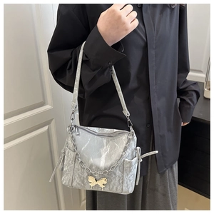 Silver wrinkled metallic handbag featuring a chain strap and butterfly charm worn by model