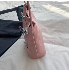 Detail view of pink leather tote bag featuring decorative silver bows and side structure