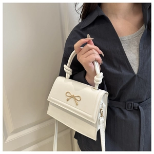 Detail of white leather handbag with golden bow buckle and knotted handle texture