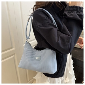Detail of light blue shoulder bag featuring fine vertical pleated texture and brand tag