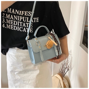 Detail of light blue crossbody bag with top handle and brown leather pendant charm