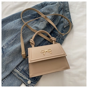 Close-up of beige trapezoid bag with golden metal bow detail and knotted handle design