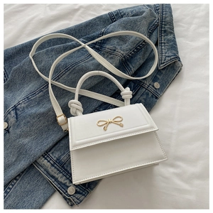 Detail of white leather shoulder bag with gold bow clasp and knotted handle on denim