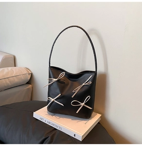 Detail of black faux leather bucket bag with four 3D cream bow accents on a book