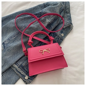 Detail of rose red handbag featuring a gold bow ornament and knot handle design