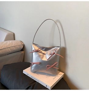 Detail of silver metallic shoulder bag featuring four pink ribbon bows on a white art book