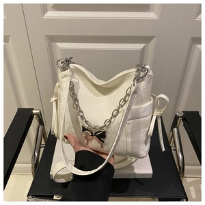 Close-up of white shoulder bag with metallic chain and stylish butterfly pendant detail