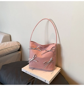 Detail of pink shoulder bag with silver bow accents on an art book in a modern home