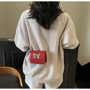 Detail of red mini crossbody bag with silver bow ornament and chain strap on a model