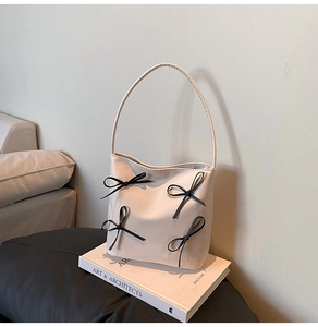 Detail of cream white bucket bag with black bow accents on an art book background