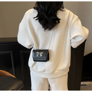 Detail shot of a black chain bag with a silver bow clasp on a white dress