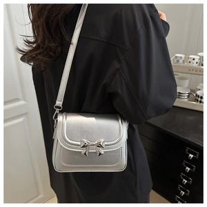 Detail of silver crossbody bag with metallic finish and bow buckle worn by a model