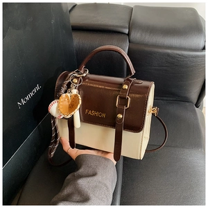 Detail of a mini two-tone brown and beige crossbody bag with a baseball glove charm