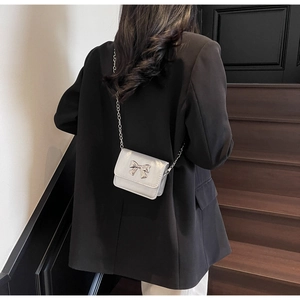 Detail of a mini silver chain bag with a metal bow accent on a black suit jacket