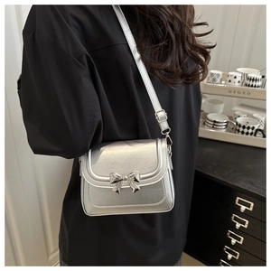 Detailed view of silver crossbody bag with metallic bow and adjustable strap on a model