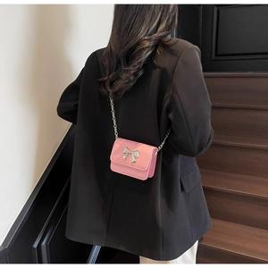 Model wearing a pink leather crossbody bag with a silver bow clasp and chain strap