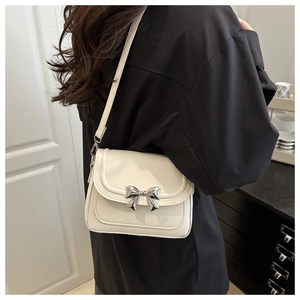 Detail of white crossbody bag featuring a stylish silver metal bow on the front flap