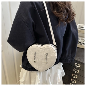 Detail of white heart-shaped crossbody bag with crocodile texture and silver chain tassels