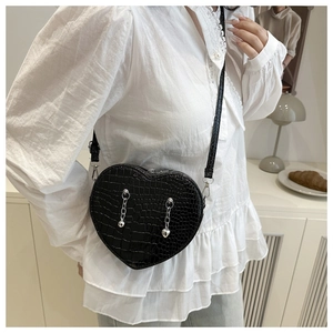 Detail view of heart-shaped crossbody bag with crocodile texture and silver chain charms