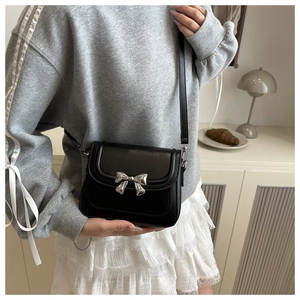 Detail of a chic black crossbody bag featuring a silver bow buckle on casual outfit