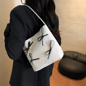 Minimalist white faux leather shoulder bag with decorative black bows on a model