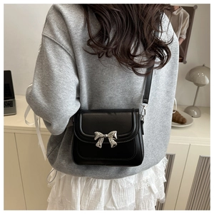 Lifestyle view of a black crossbody bag with silver bow hardware worn by a model