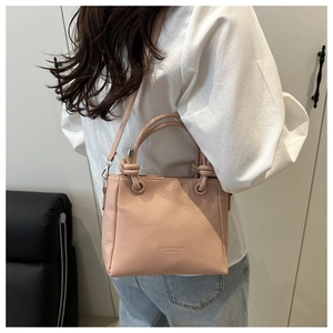 Side view of a light pink bucket bag with knotted handles and embossed leather texture