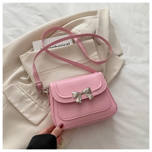Detailed view of pink PU leather crossbody bag with silver bow buckle on beige blazer