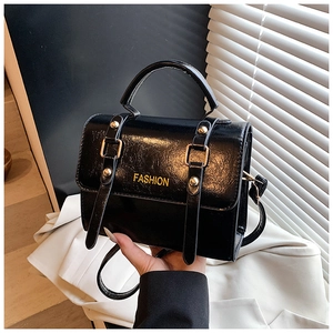 Detail of black patent leather crossbody bag with gold hardware and FASHION lettering
