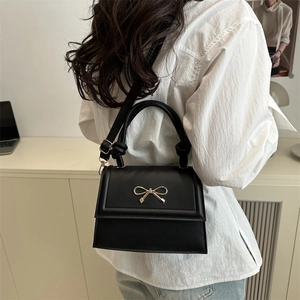 Elegant black faux leather shoulder bag with golden bow hardware and a sleek flap design