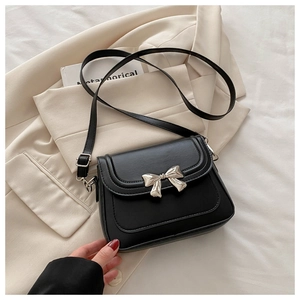 Detailed shot of a black crossbody bag featuring a 3D silver bow accent and fine stitching