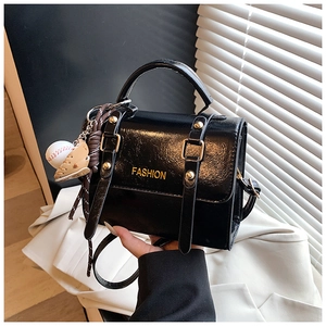 Detail of black patent leather crossbody bag with gold FASHION text and baseball charm