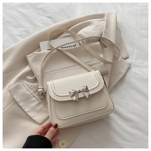 Detail of a creamy crossbody bag with a silver metal bow buckle on a beige blazer
